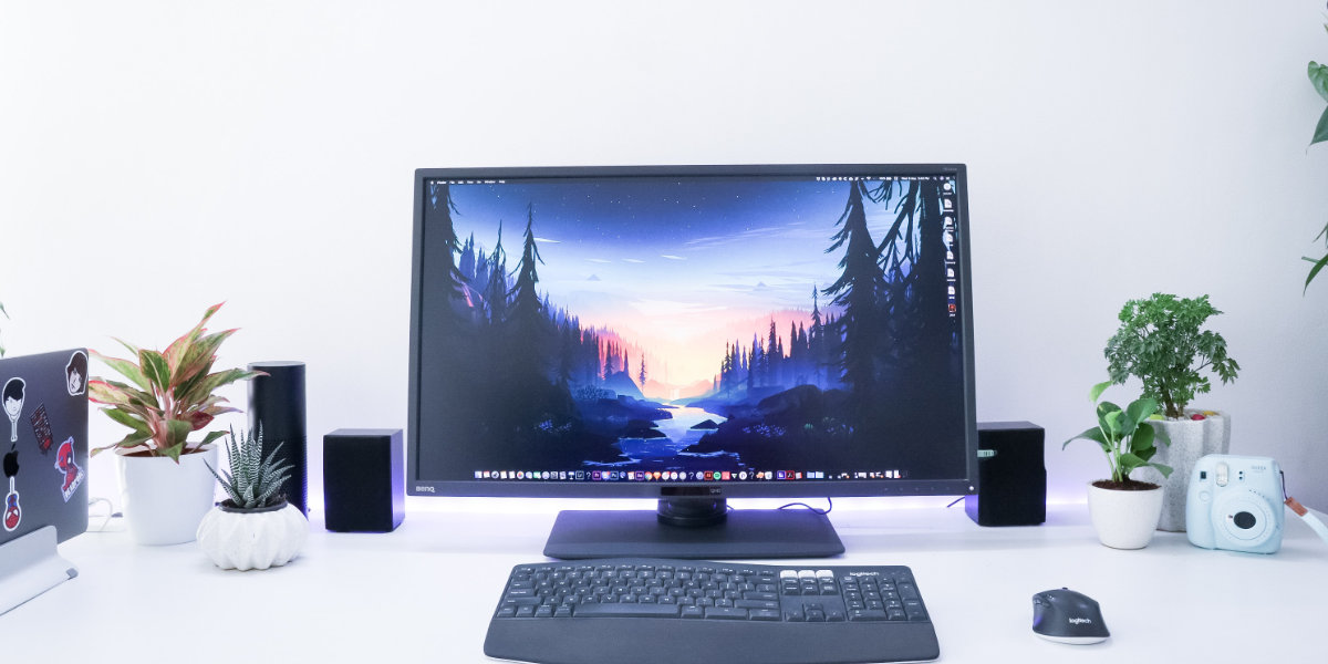 a modern computer setup with a monitor displaying a scenic landscape, keyboard, and plant decorations